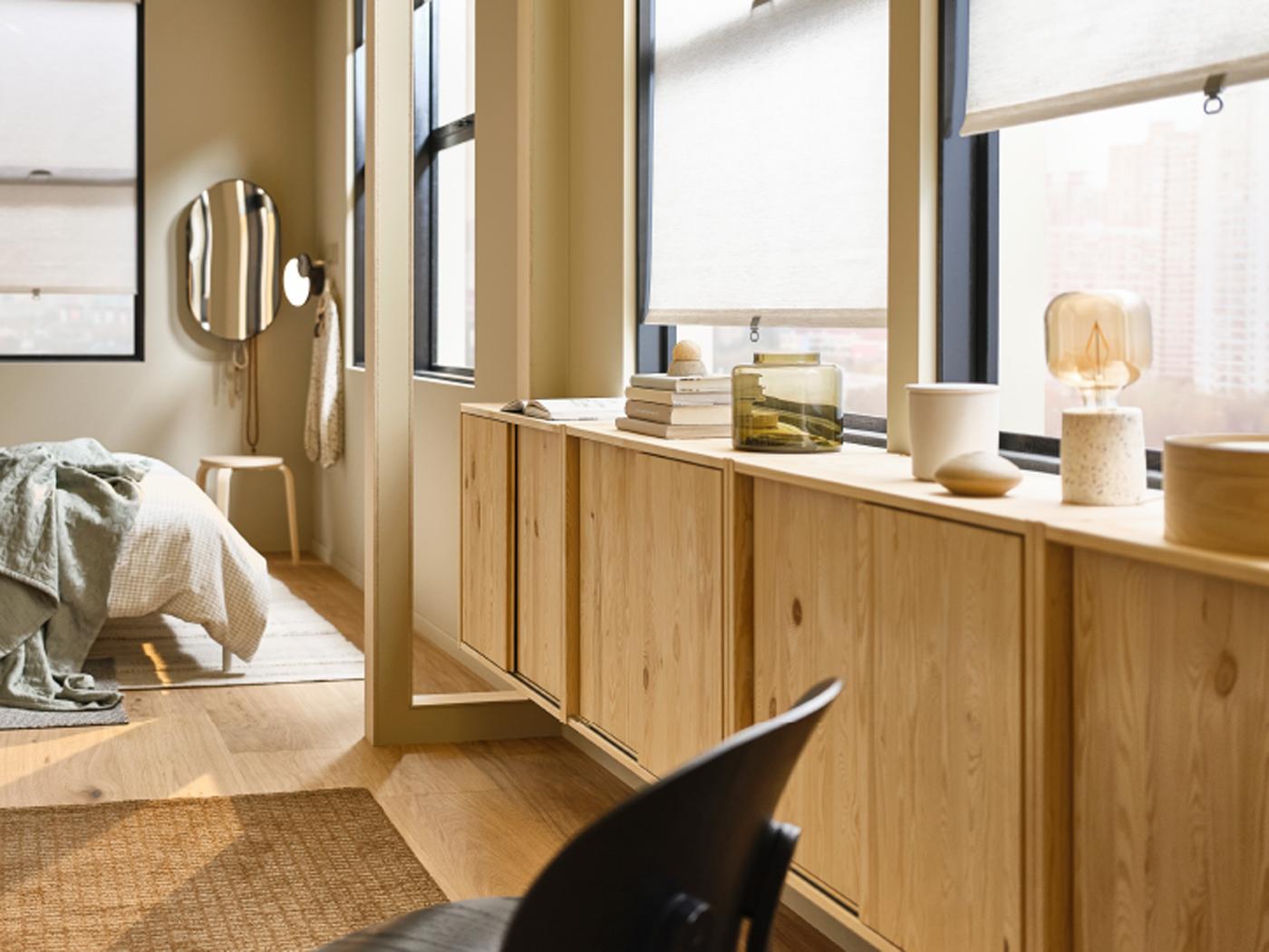 A pine IVAR cabinet with sliding doors with objects on top in a light bedroom with SANDVEDEL roller blinds on the window.