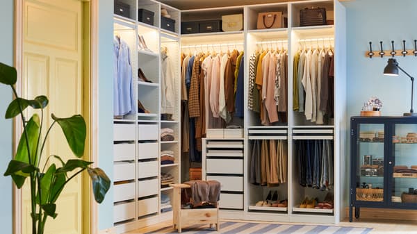 A pine PERJOHAN stool with storage stands in front of a large open PAX corner wardrobe with clothes, shoes, boxes and bags.