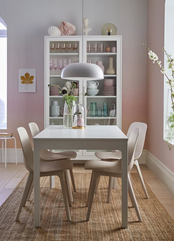 A pink and white dining area with an EKEDALEN white extendable table surrounded by curved ODGER white and beige chairs.