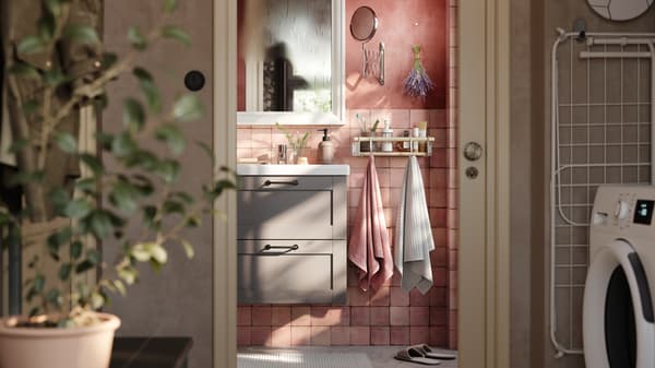 A pink bathroom with a grey ENHET washstand with two drawers, a white mirror and two towels hanging from a rail with hooks.