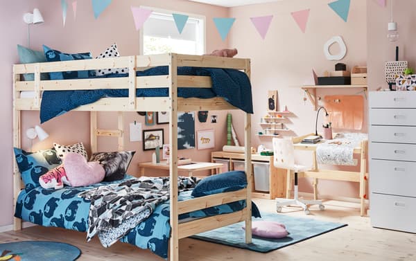A pink bedroom with pine bunkbeds featuring blue animal printed textiles and a wood desk.