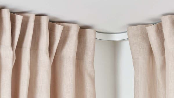 A pink curtain on a white VIDGA curtain track that goes around the corner.