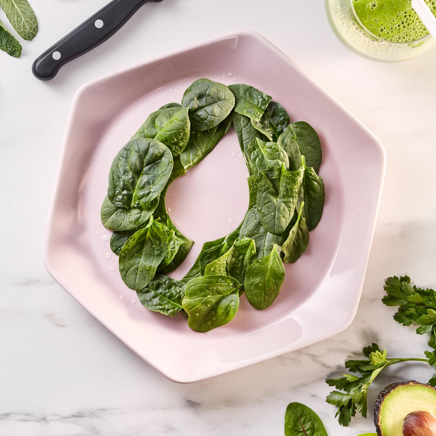 A pink hexagonal plate on white marble bench top. On the plate are baby spinach leaves decoratively arranged in a ring.