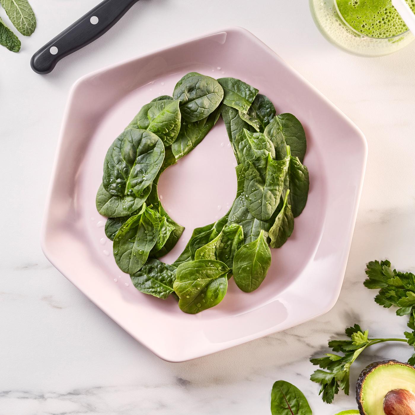 A pink hexagonal plate on white marble bench top. On the plate are baby spinach leaves decoratively arranged in a ring.