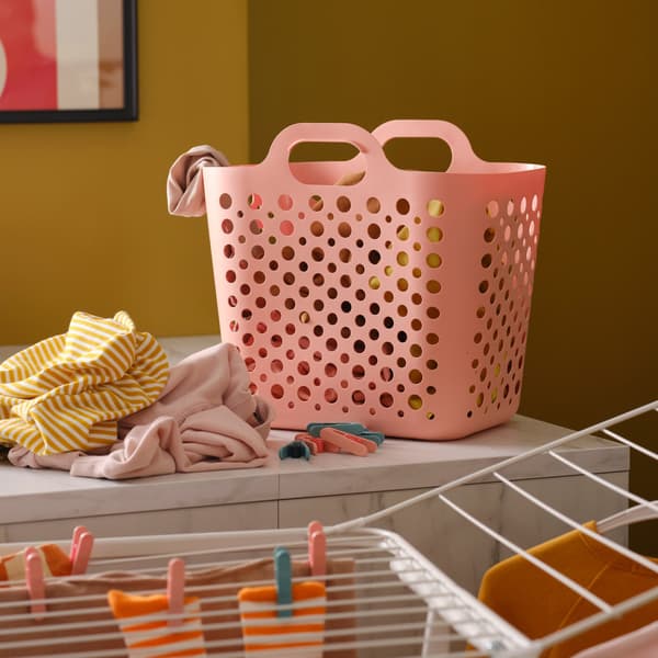A pink SLIBB flexible laundry basket and a pile of clothes on a kitchen worktop, plus a white drying rack with more clothes.