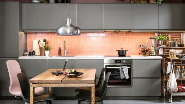 A pink-tiled kitchen with dark grey kitchen fronts, anthracite chairs, a dining table in oak veneer and a VÄXJÖ pendant lamp.
