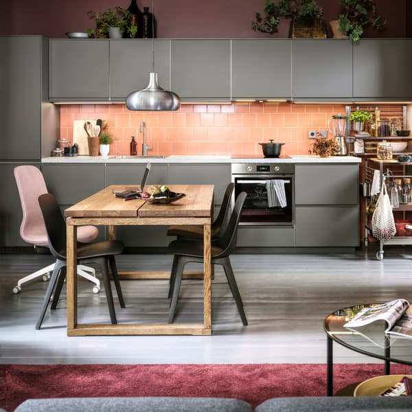 A pink-tiled kitchen with dark grey kitchen fronts, anthracite chairs, a dining table in oak veneer and a VÄXJÖ pendant lamp.