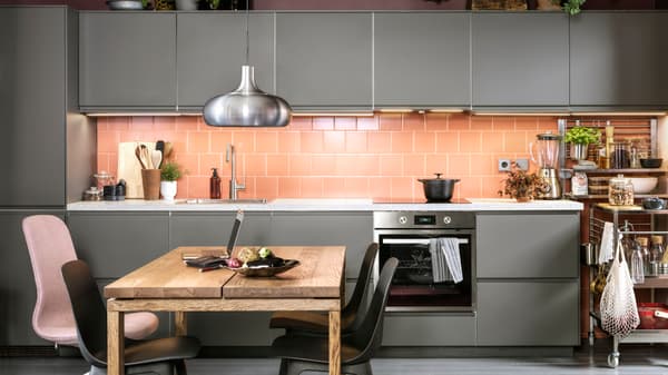 A pink-tiled kitchen with dark grey kitchen fronts, anthracite chairs, a dining table in oak veneer and a VÄXJÖ pendant lamp.