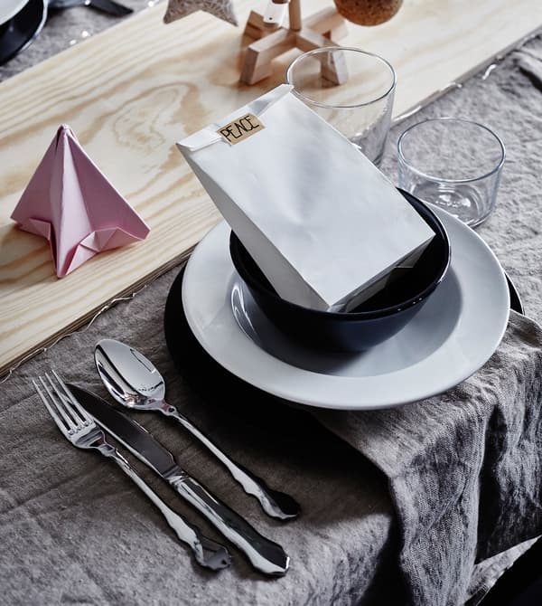 A place setting with white and black flatware, paper decorations and a wooden board as a table runner.