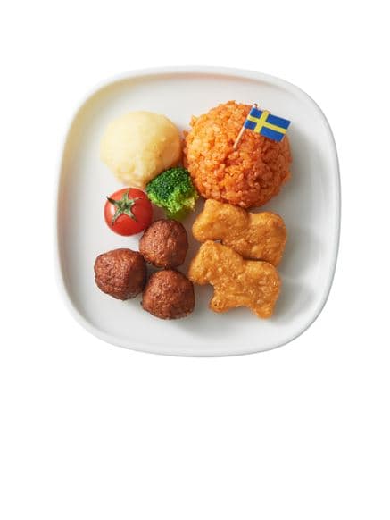 A plate of assorted food items including meatballs, mashed potatoes, broccoli, a cherry tomato, chicken nuggets, and a portion of rice topped with a Swedish flag toothpick.