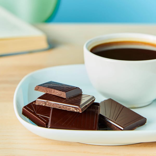 A plate of chocolate pieces and a cup of coffee on a wooden surface.