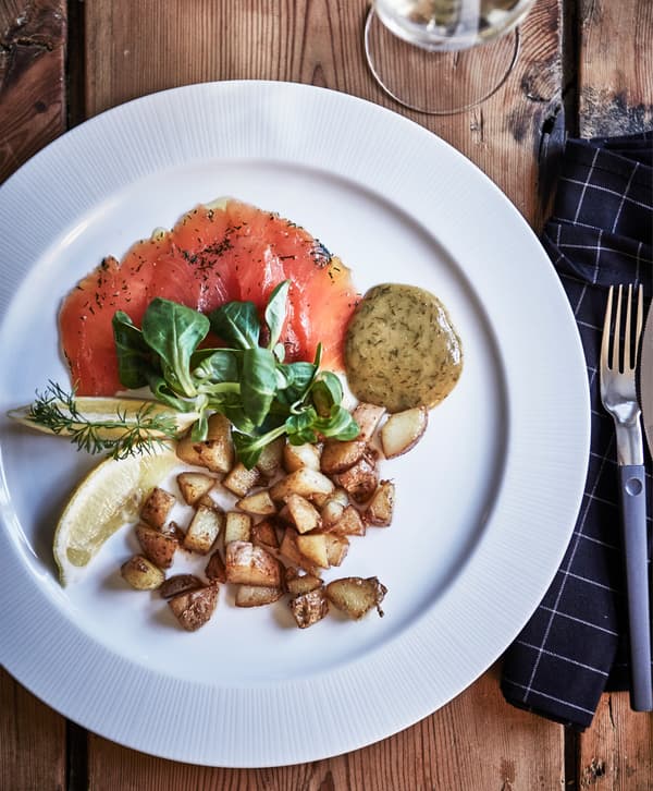 A plate of salmon, pickles, potatoes, mustard