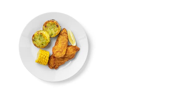 A plate with a portion of vegetable medallions, a piece of corn, a slice of lemon and two chicken nuggets.