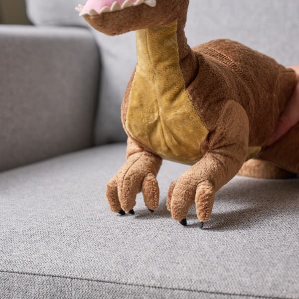 A plush dinosaur toy sitting on a gray sofa, showing its legs and part of its body.