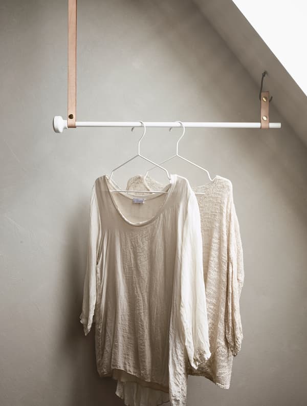 A pole hung from leather straps attached to a sloped ceiling holds clothing on hangers.