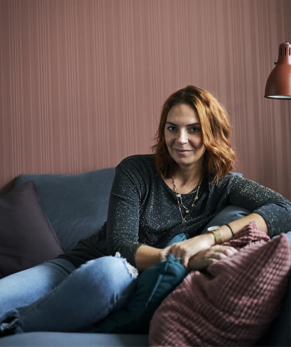 A portrait of Amélie sitting on a grey sofa against a red wall.