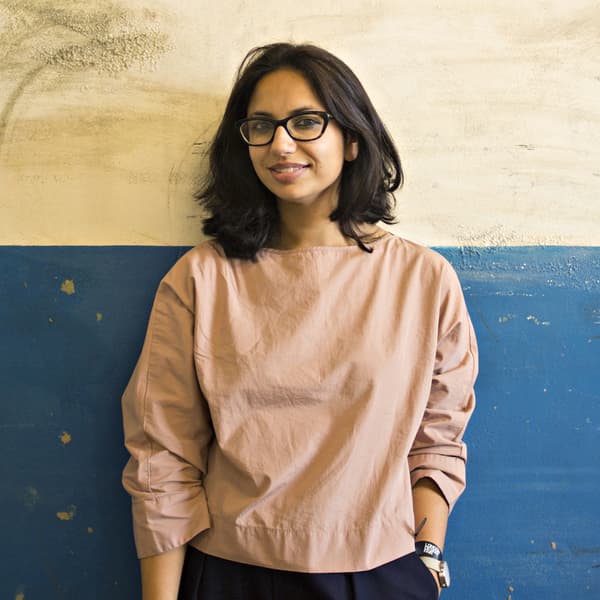 A portrait of Kangan Arora standing against a rough wall.
