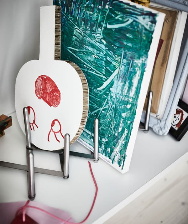 A pot lid organiser inside a kitchen cabinet, displaying a young artist's work.