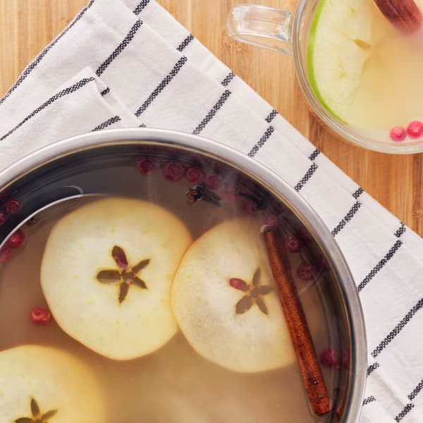 A pot of warm FLÖJT green tea with apple slices and spices on a striped cloth with a mug on the side.