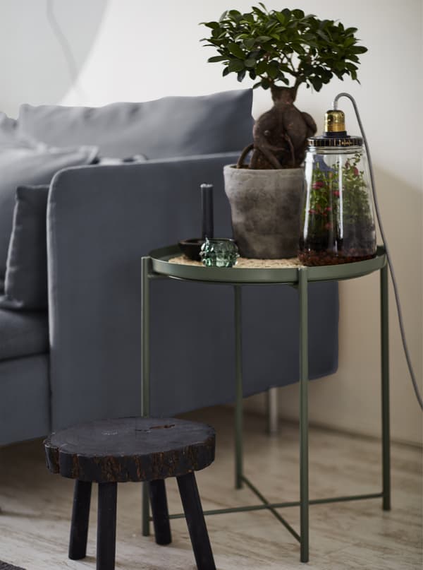 A pot plant on a tray table next to a grey sofa.