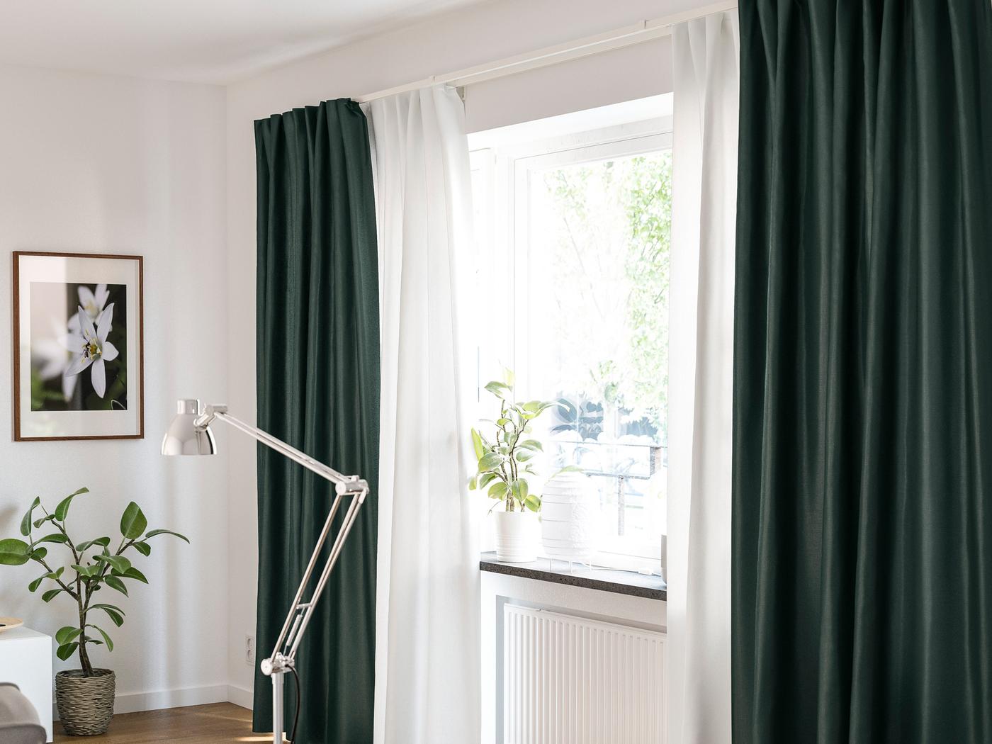 A potted plant and a lamp stand on the sill of a window that has two layers of curtains, one sheer and one thick.