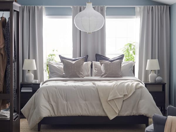 A primary bedroom with gray curtains and a white lampshade above a neatly made bed with decorative pillows on it.