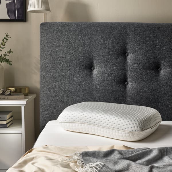 A RAMSLÖKSMAL pillow placed on a bed with its cooling side face updwards. 3 light blue snowflakes are present at the top right of the pillow and a circular picture showing the 3 layers of the pillow is seen at the bottom left corner of the picture.