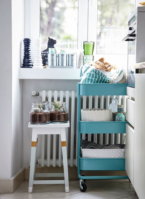 A RÅSKOG trolley and a white stool provide flexible, moveable storage in this bright but tiny kitchen.
