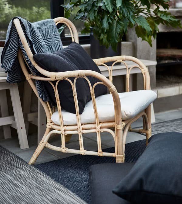 A rattan armchair with a white cushion and black back pillow.