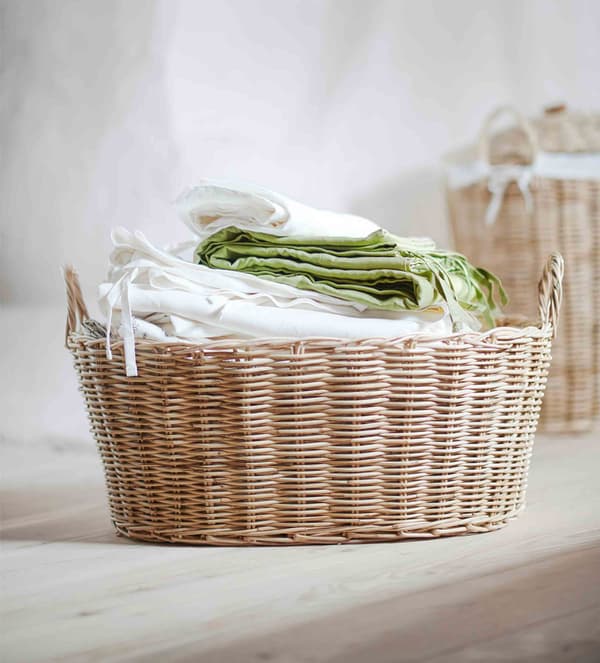 A rattan basket piled high with natural-feeling textiles.