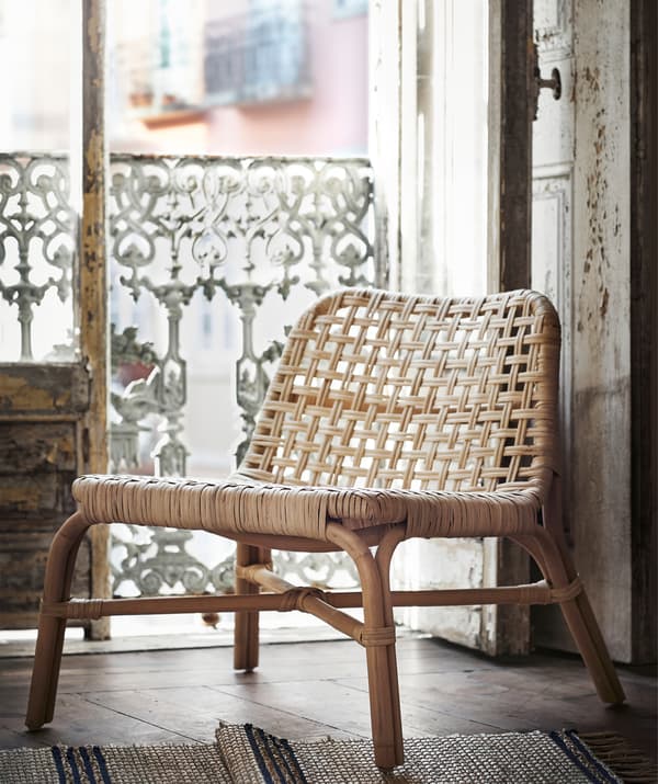 A rattan chair standing in the doorway of a rustic balcony.