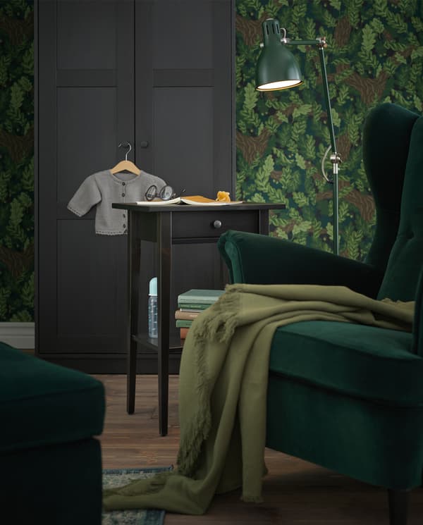 A reading corner with a green wing chair, a green floor lamp and a HEMNES bedside table used as a side table.