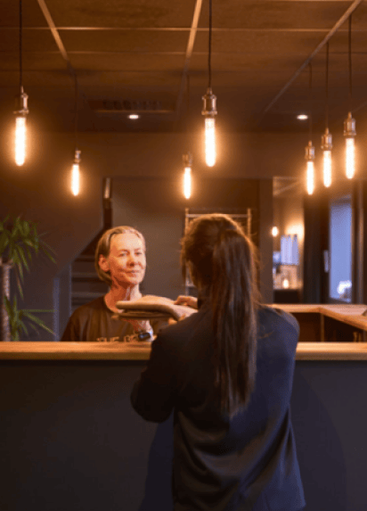 A receptionist welcoming a customer at a front desk, light hanging from the ceiling in the background.