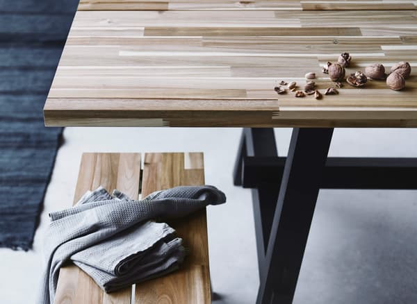 A rectangular, Scandinavian style SKOGSTA dining table and bench made from wood with grain and color variations.