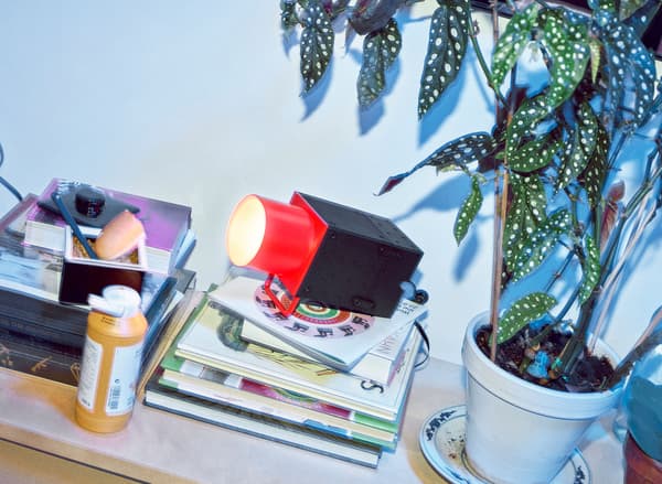 A red and black spotlight sitting on a stack of books with a plant nearby and a bottle of yellow mustard.