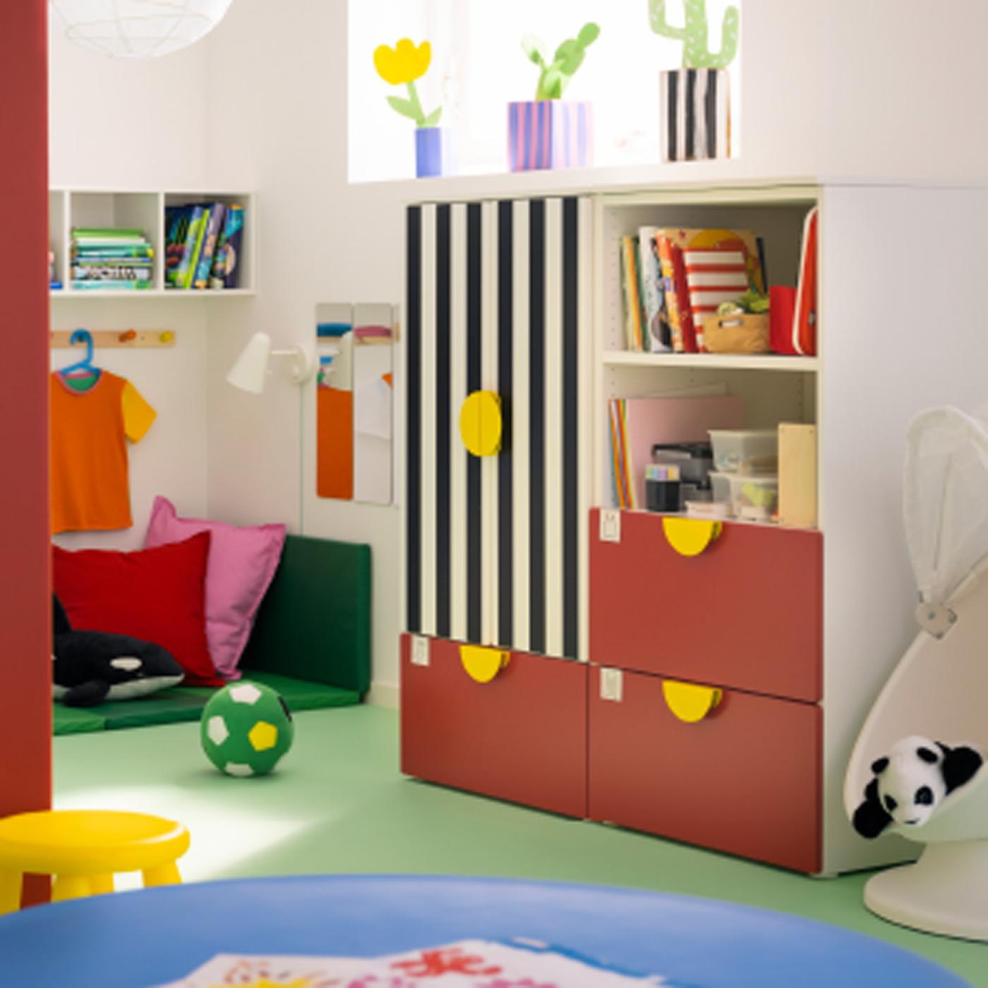 A red and striped SMÅSTAD/PLATSA storage combination with three drawers stands in a child’s room with a green floor.