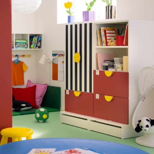 A red and striped SMÅSTAD storage combination with three drawers stands in a child’s room with white walls.