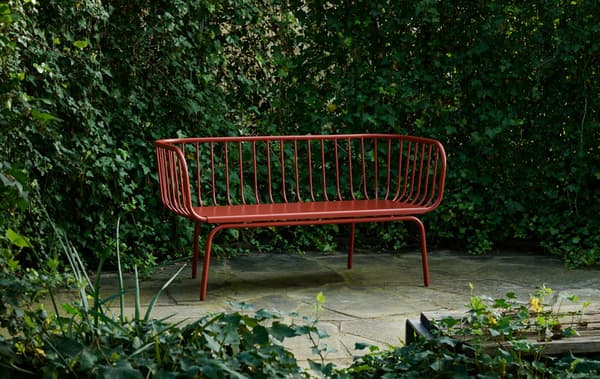 A red bench surrounded by greenery on a paved area.