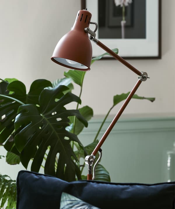 A red/brown floor lamp in a room with plants.