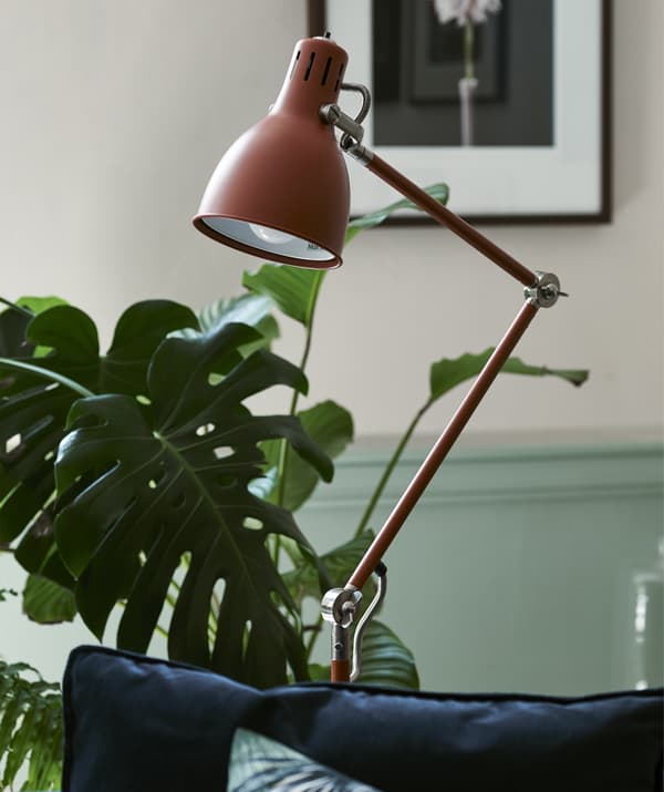 A red/brown floor lamp in a room with plants.