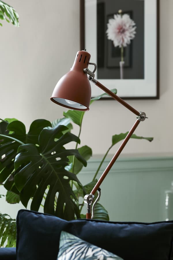 A red/brown floor lamp in a room with plants.