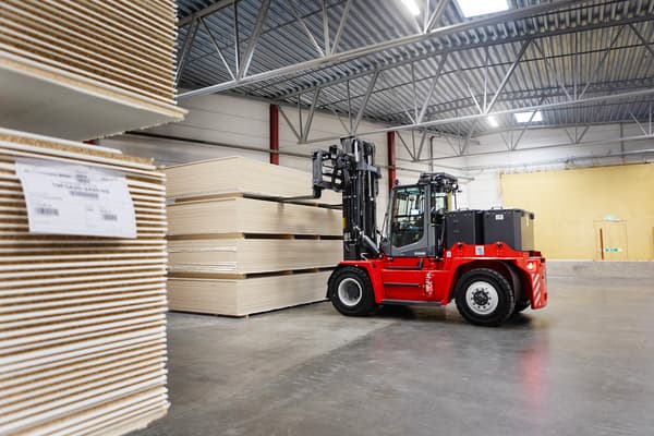 A red electric forklift lifts large packages of particleboards.