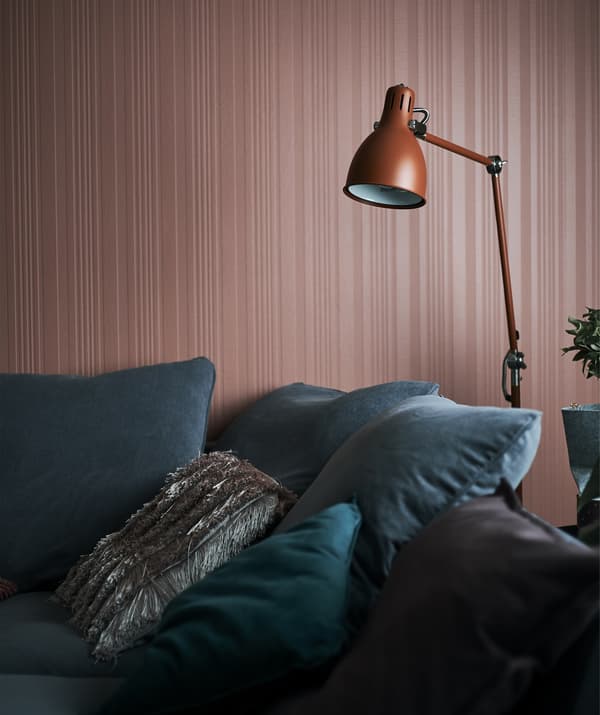 A red floor lamp hangs over a grey sofa next to a red wall.