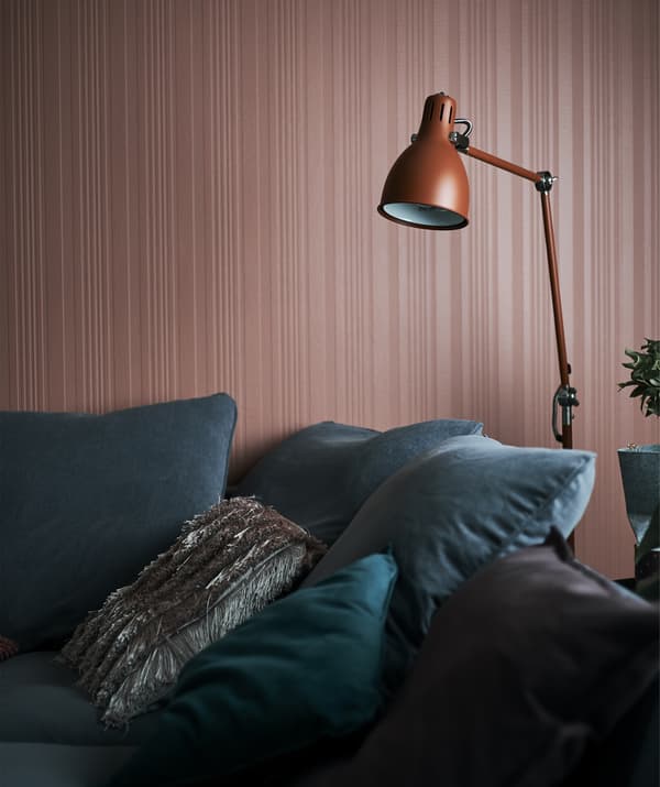 A red floor lamp hangs over a grey sofa next to a red wall.