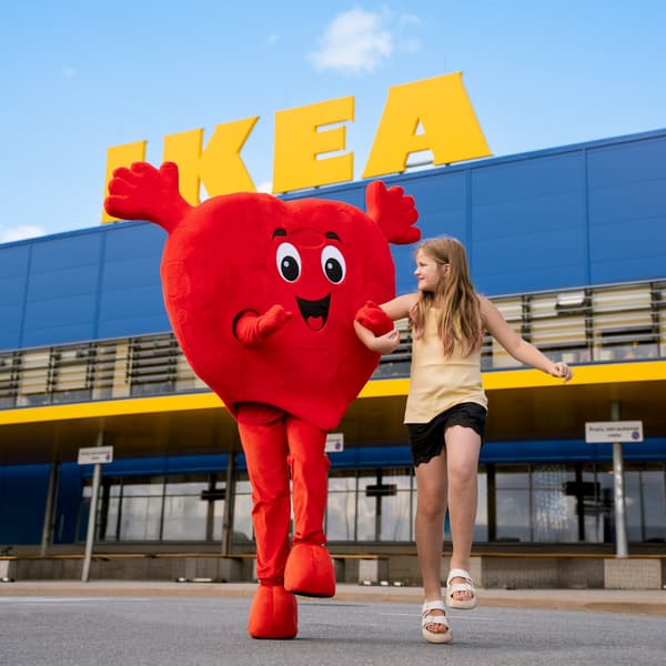 A red Heart mascot and a girl in a yellow T-shirt and black shorts walk hand in hand, with an IKEA store in the background.				