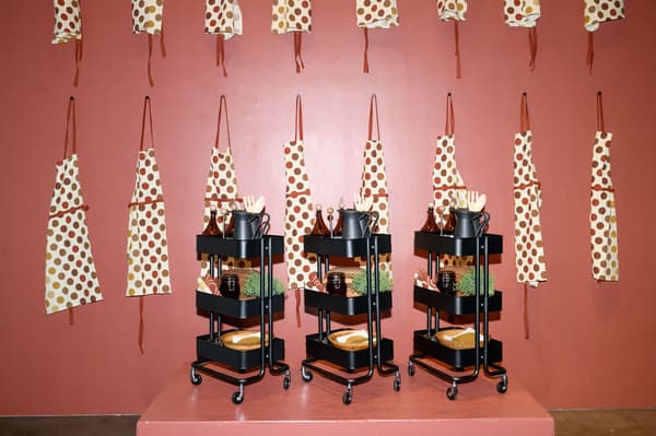 A red wall with several aprongs hanging and dark storage carts in front.