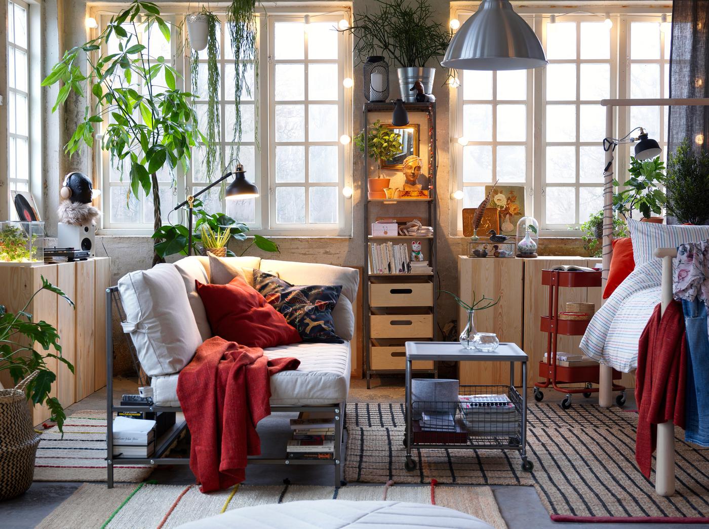 A relaxed living room with white sofa with books and other stuff on a built-in shelf beneath, jute rugs and plants.
