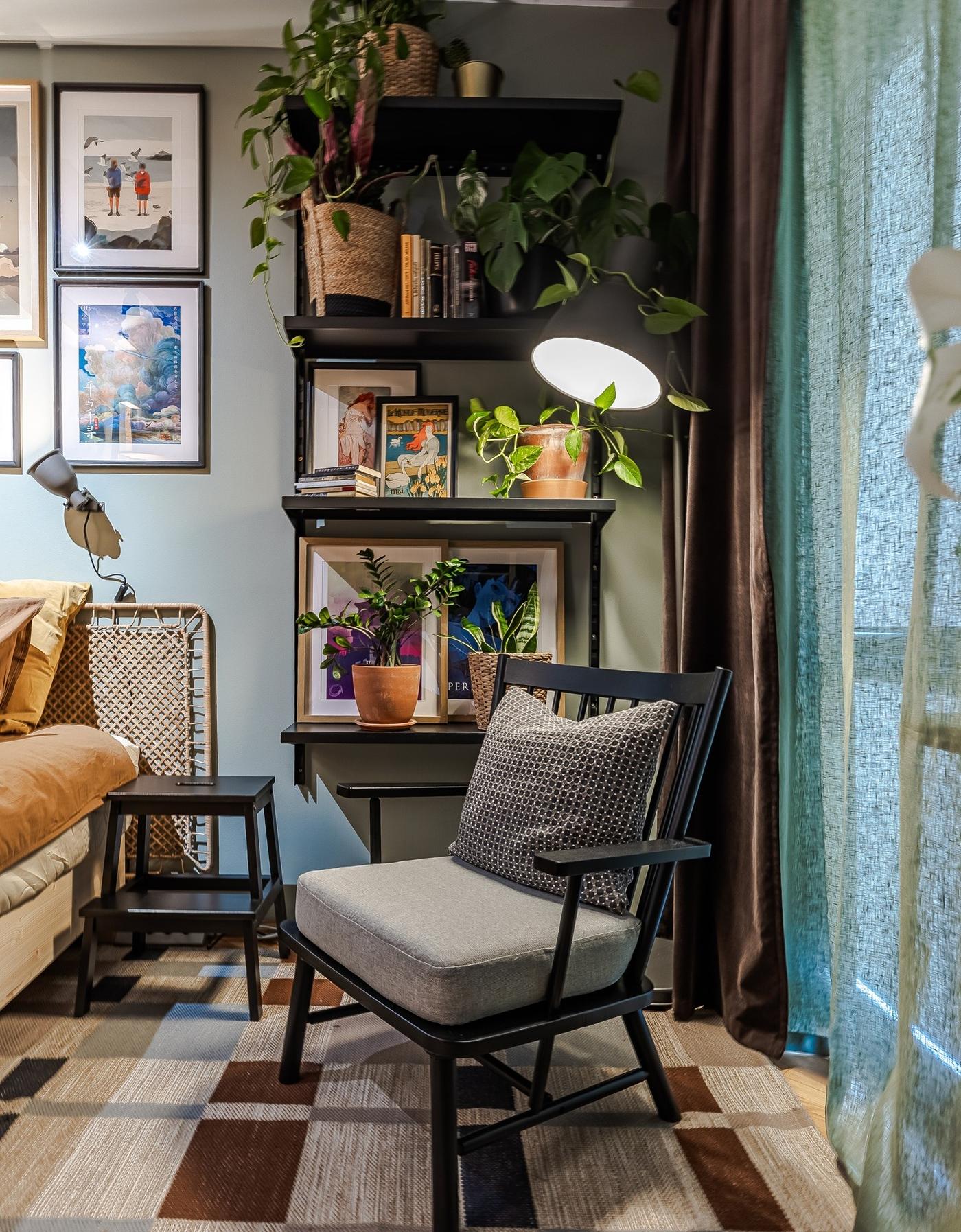 A relaxing corner by the window with an armchair, a checked rug and black metal shelving filled with plants.