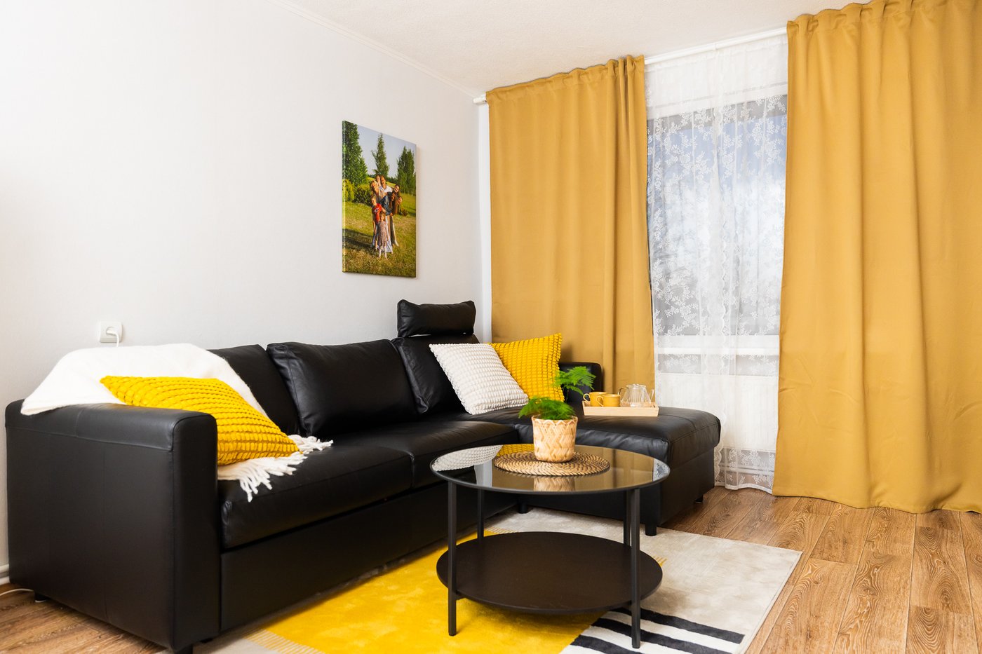 A renovated living room featuring a sofa, a round coffee table, and yellow textile accents. The room shows a cosy atmosphere and a thoughtful furniture layout.
