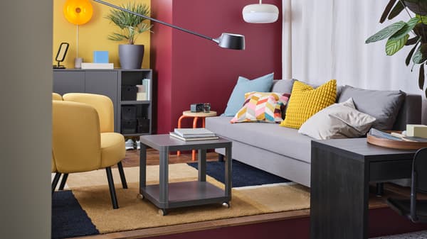 A retro inspired living room with a large grey ÄLVDALEN sofa-bed, yellow armchair, grey coffee table and bold painted walls.